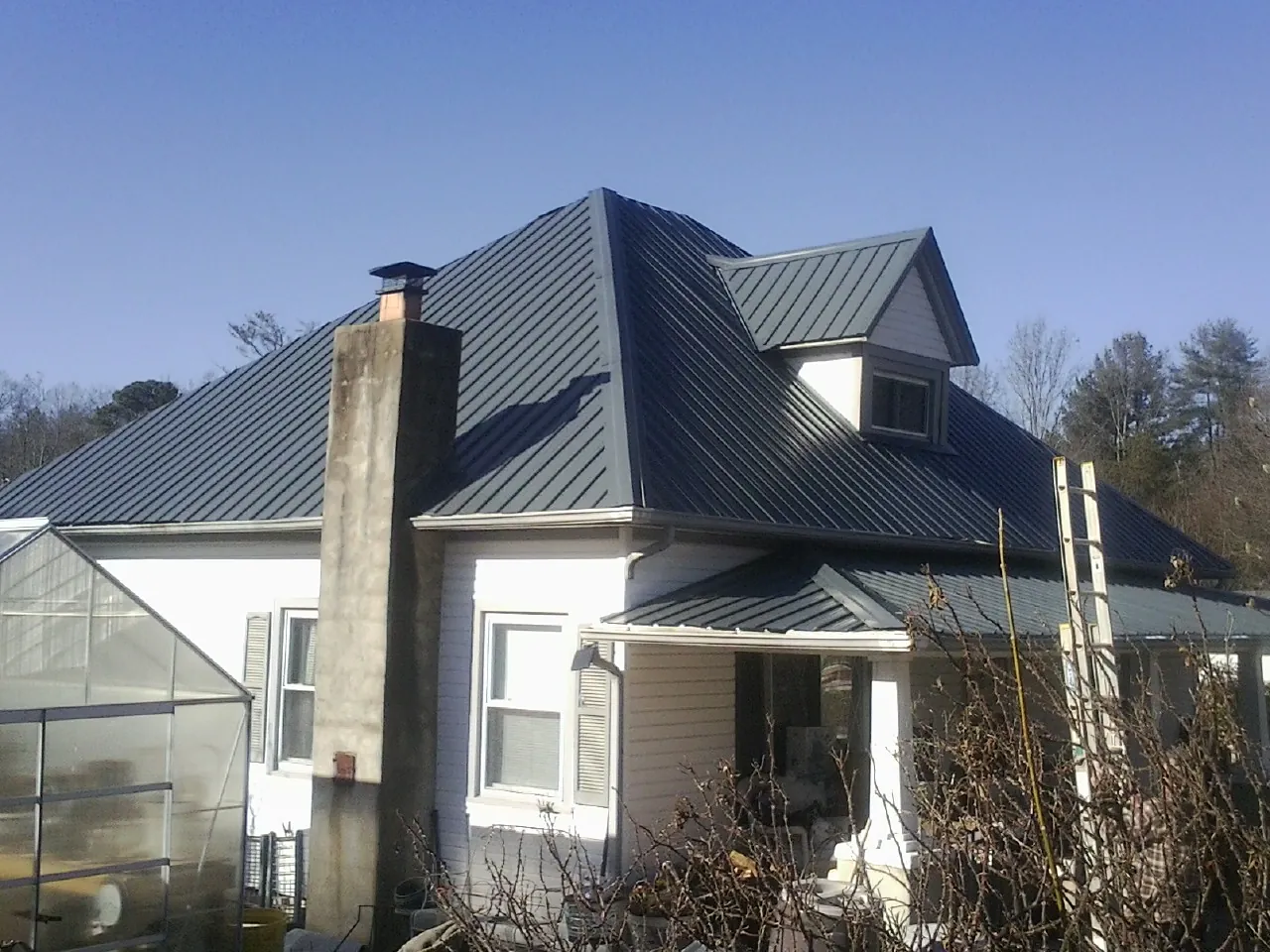 Dark blue standing seam metal roof on a white farmhouse with dormer — Slate & Tile Roof Repair by Roofing Brothers in Vidor