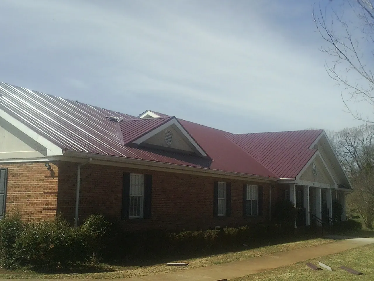 Red metal roof with gabled entries on a long brick building, from a Hail Damage Roof Repair job in Vidor