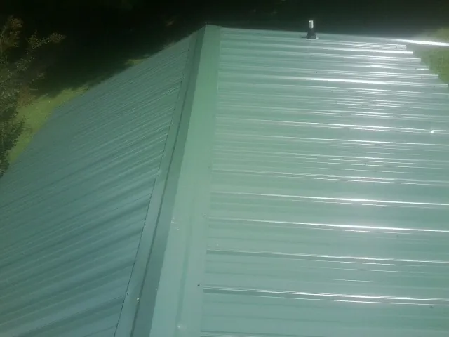 New green metal panels meeting at the ridge of a roof — Flat Roof Repair work by our crew in Vidor